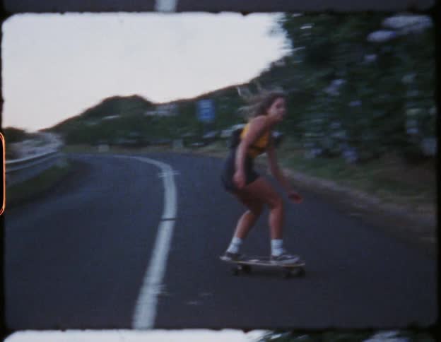 A young woman rides her skateboard back and forth across a two lane highway