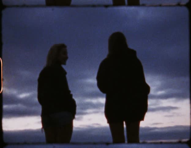 Two women wearing thick coats stand and converse while looking out over the horizon
