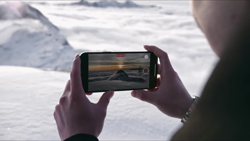 A woman stands outside taking a picture with her cell phone of the winter landscape
