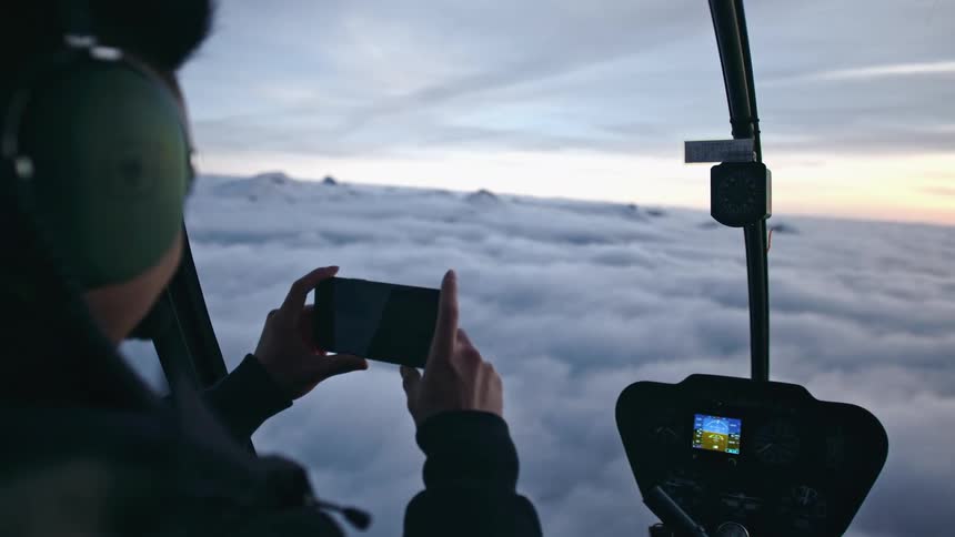 People sitting in cockpit of air transport view sky over cloud layer and one takes picture with mobile phone