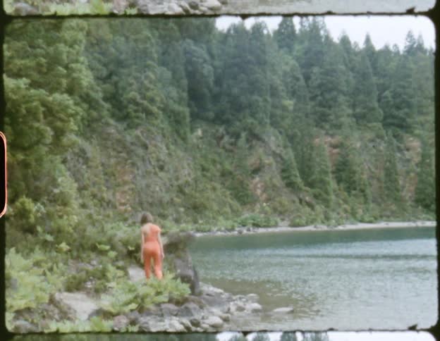 Woman walking on a path next to a river at daytime alongside a cliff covered in bushes and trees