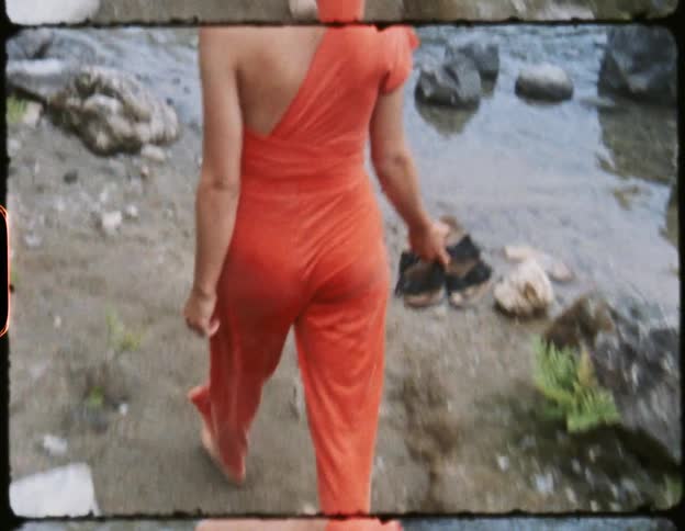 A young woman walks barefoot along a small dirt path next to a river