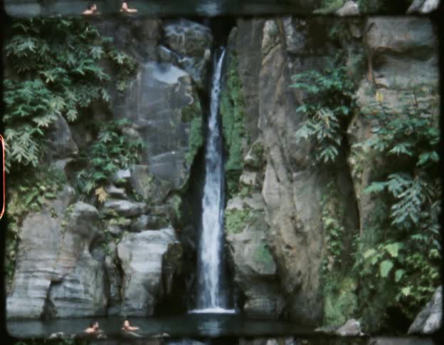 A vintage film of a man and woman in a river at the bottom of a waterfall