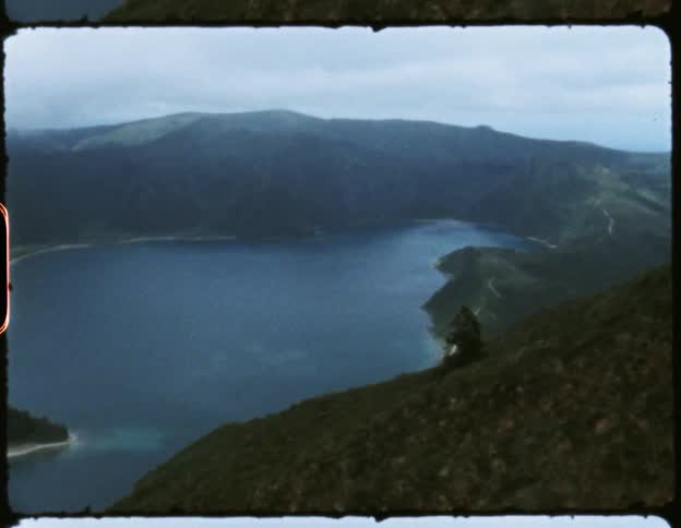 Lake enclosed by lush green mountains at daytime leading out to a river