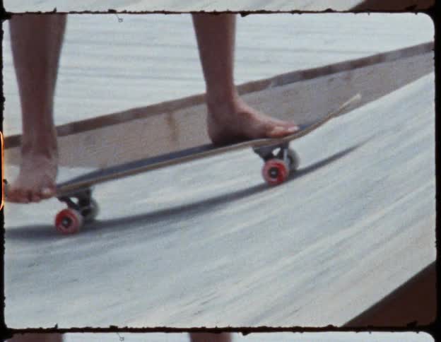 A person stands on a skateboard as it moves up a plywood ramp outdoors