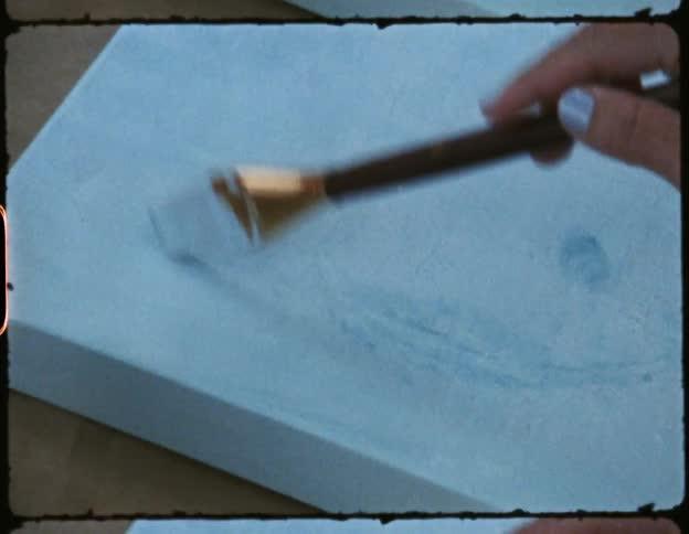 On a small canvas a female repeatedly taps a paint brush as she works on a painting