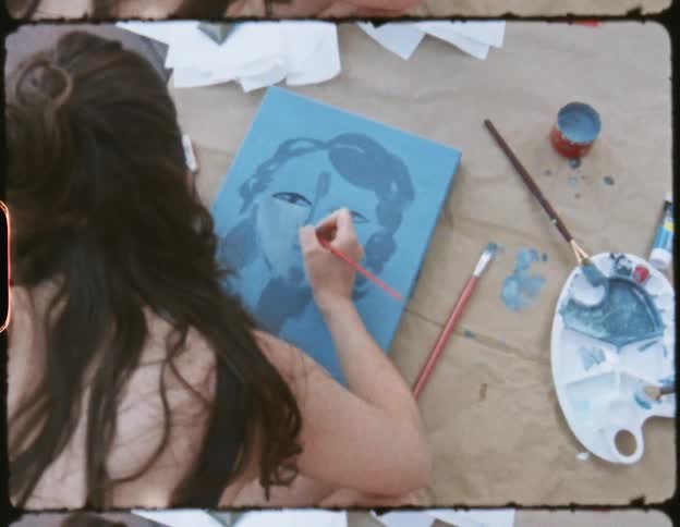 Two woman sitting on the floor with paint supplies painting with paint brushes on small canvases