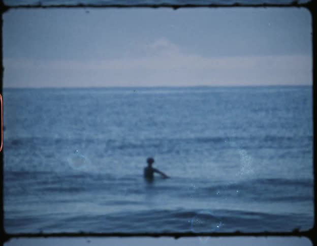 Man swimming out in the ocean as waves pass under him during the day