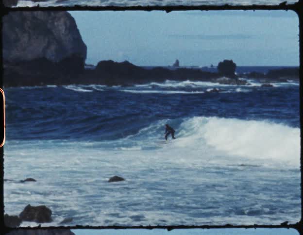A person on a surfboard surfing on a wave in the ocean with the sky and clouds in the background