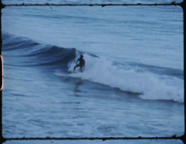 Male surfer surfs on a small wave in the ocean and then he falls off
