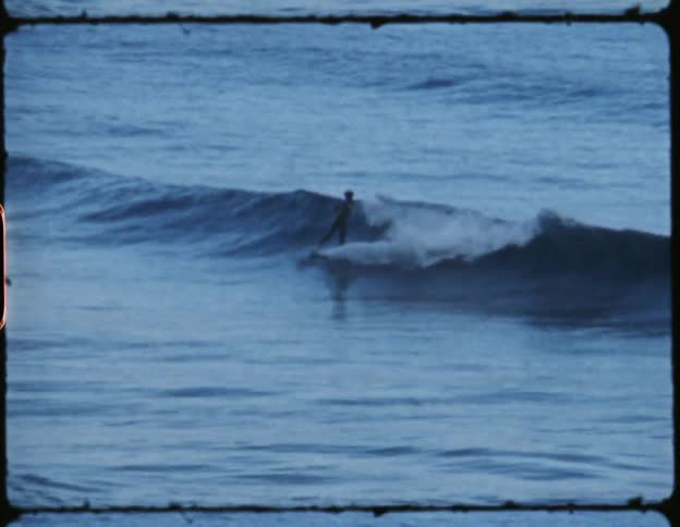 Vintage film of a surfer riding sea waves over a yellow surfboard