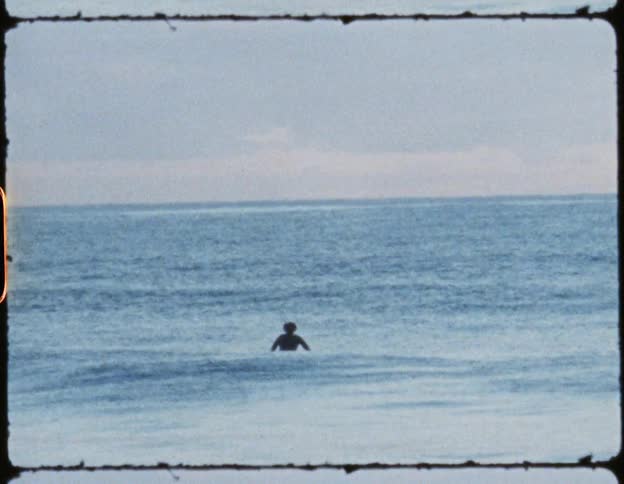 A man swimming out in the ocean at daytime close to the shore looking out to the horizon