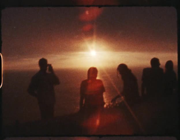 Silhouette of a group of friends on a party near the beach at sunset on film