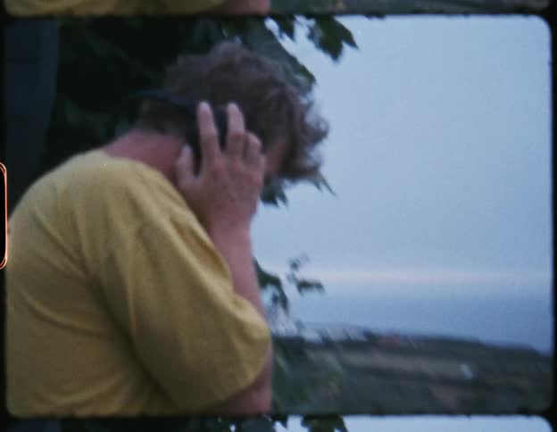 A man is dancing while wearing headphones and using his laptop outdoors