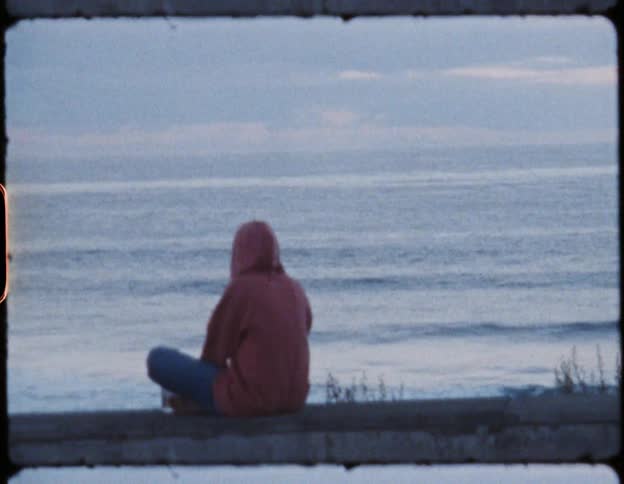 A woman sits on the ground while overlooking the ocean waves wash upon the shoreline