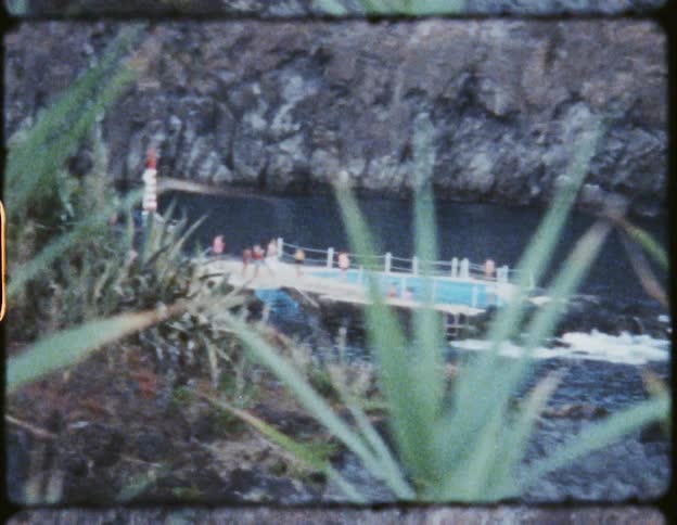 People in a swimming pool next to a river surrounded by mountain cliffs and plants