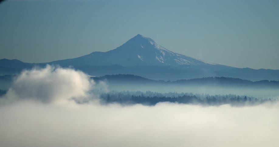 An enormous mountain stands tall as thick clouds pass in front of it