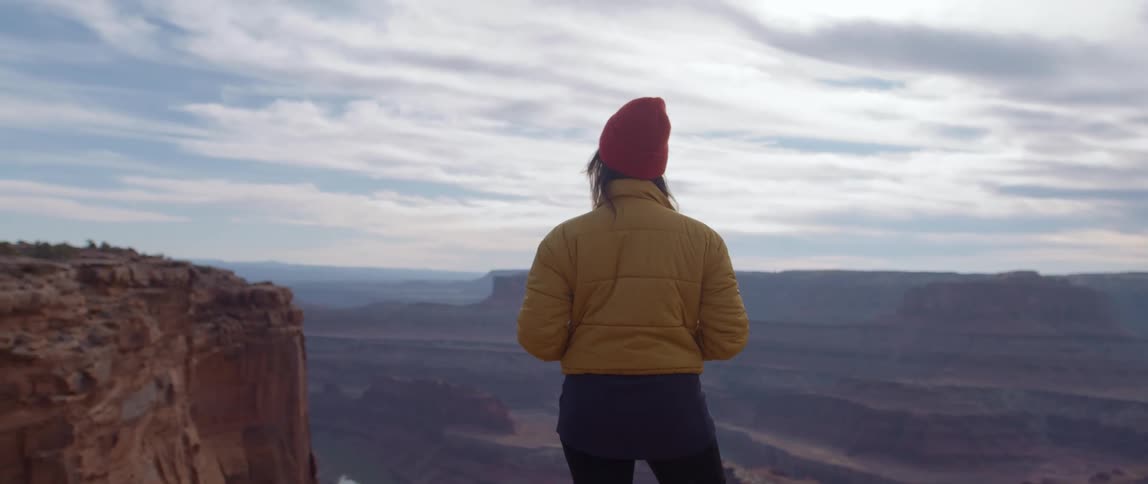 A woman stands on a rock structure and looks off into the horizon