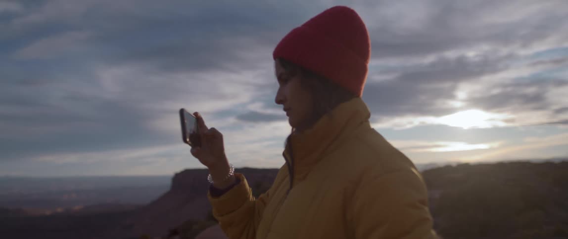 A woman wearing a warm jacket uses her phone to take a picture of the surrounding landscape