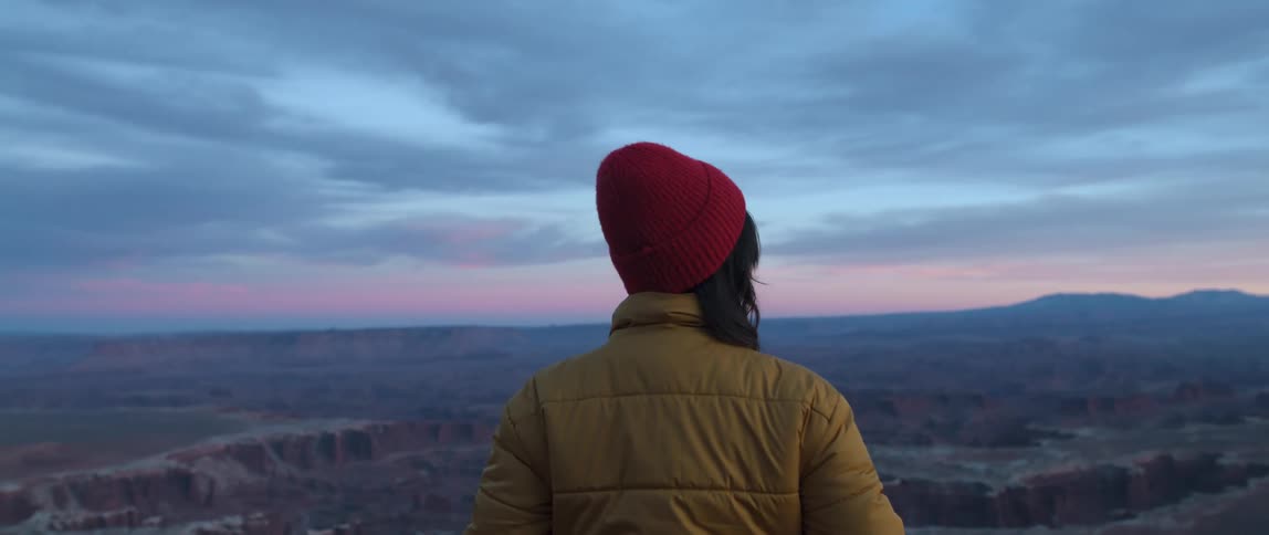 A woman stands and looks out at a canyon