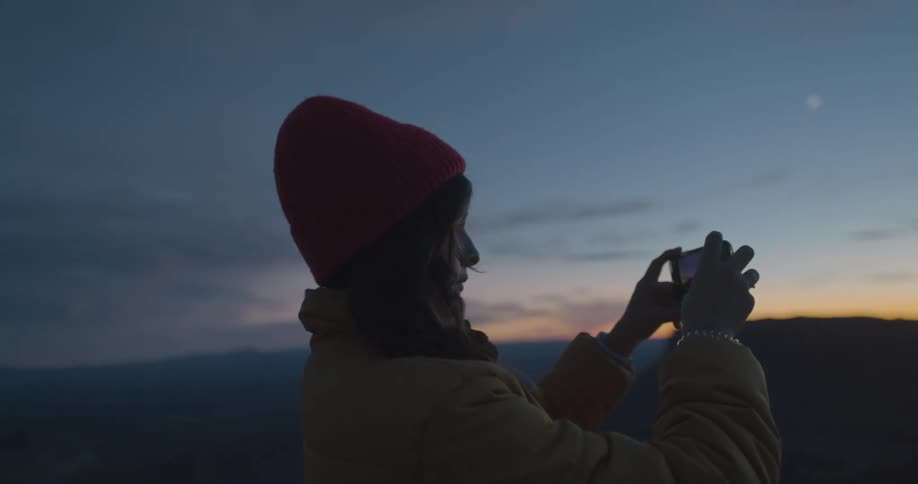 Woman taking pictures of the horizon at sunset standing on a mountain top