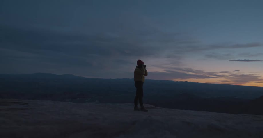 A person stands outdoors and holds up a camera to take a photograph of the landscape