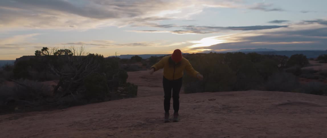 Young woman happily dancing on a mesa in the badlands at sunset