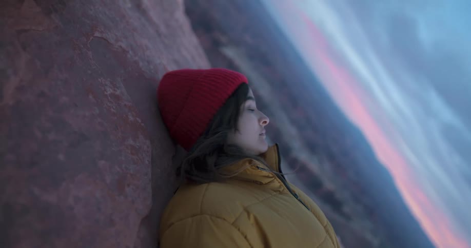 Woman lying down on a cliff looks over to her left over at the horizon at sunset