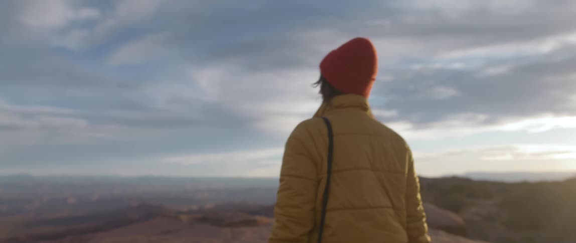 A woman tucks her hands in her coat as she walks across the summit of a canyon
