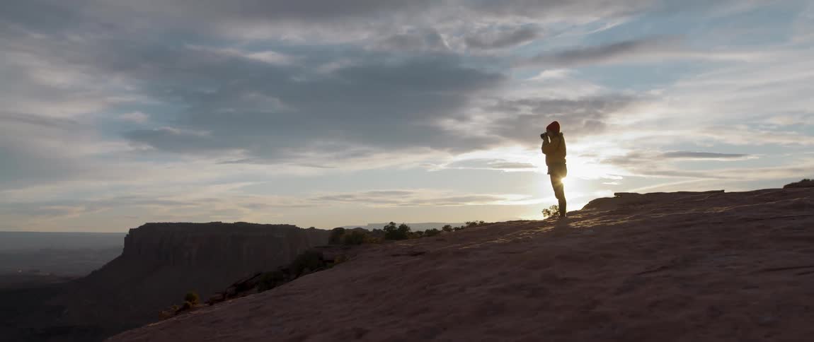 Woman stands up to take photographs of the canyons on the badlands at sunset