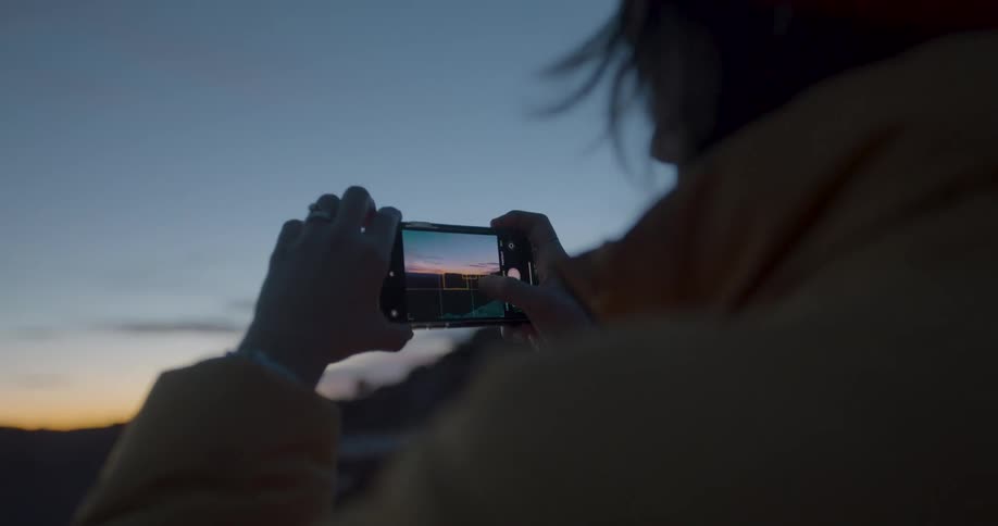 A woman is taking a panoramic photo of the sky at dusk
