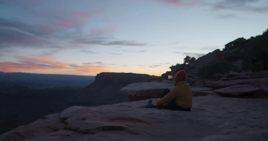 A woman uses a smart phones to take photos of the sky while sitting on a rock structure