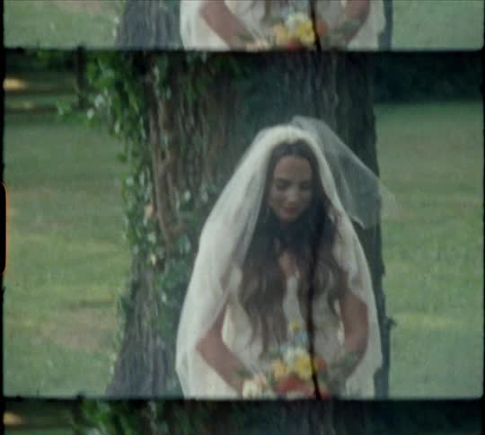 Woman wearing bridal gown and carrying bouquet poses next to large vine covered tree trunk