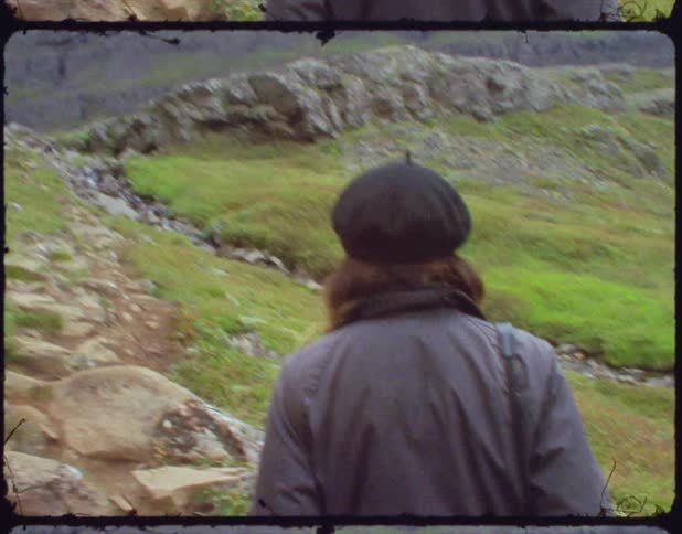 Woman with a black hat and a grey coat walks uphill on a dirt road on a cloudy day