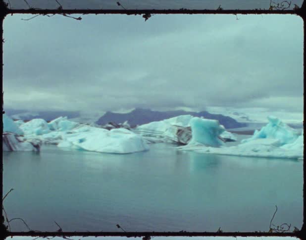 A small beach with icebergs and mountains in the background and boats in the water
