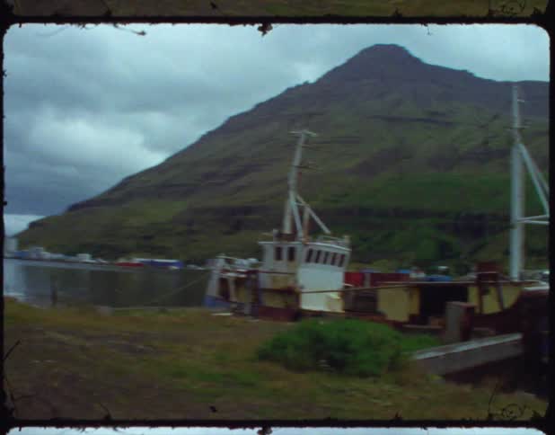 An old film with boats parked on the shore with hills in the background