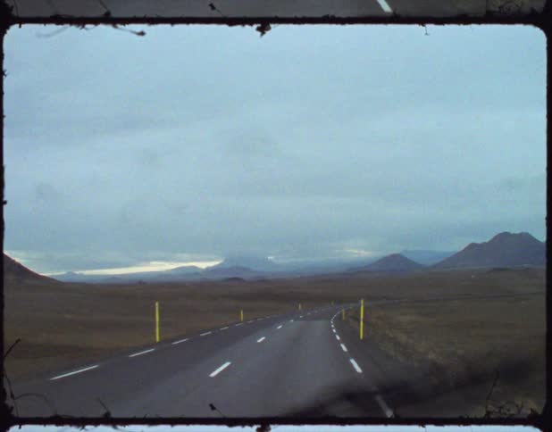 A car is driving on a road toward mountains with the windshield wipers going