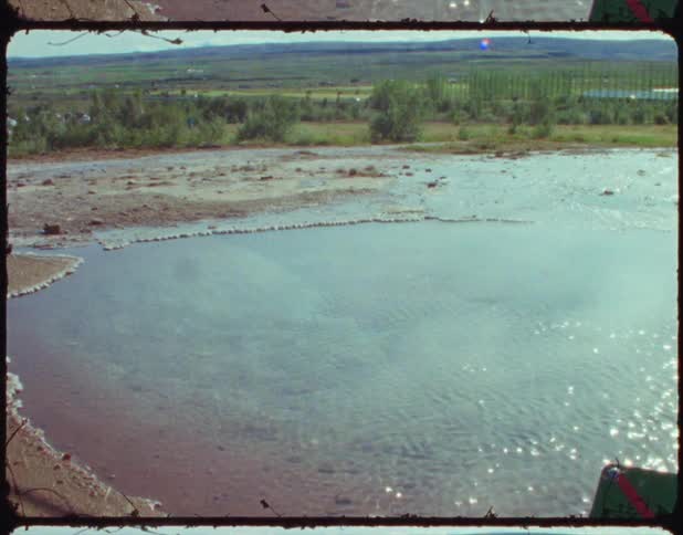 Vapor floats over rippling pond as traffic passes on road in background