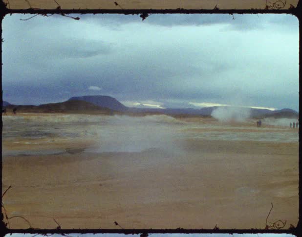 A field has smoke in the air with people walking in the background with a mountain view