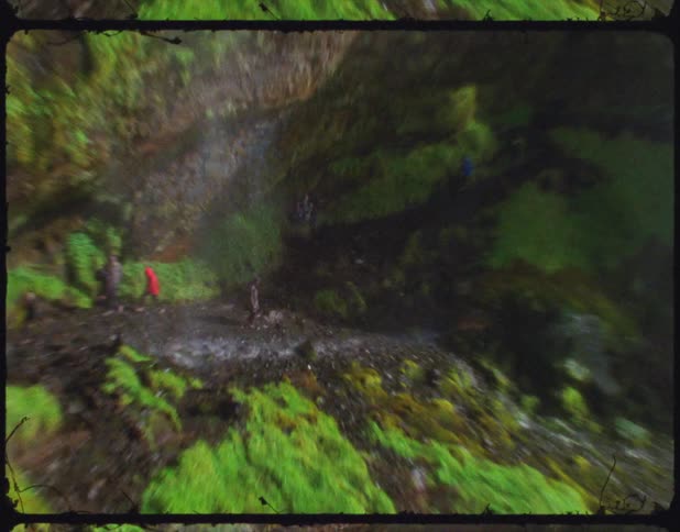 A person wearing a rain slicker looks up at a waterfall as water sprays down at them