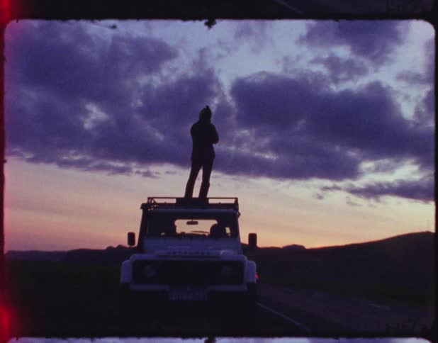 A person standing on the roof of a land rover takes pictures of the sunset