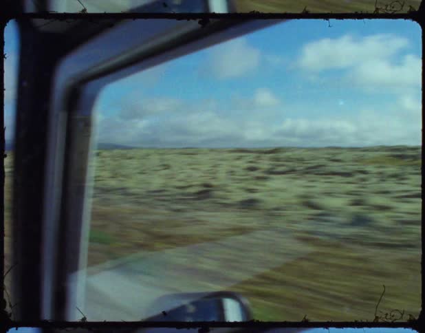 Vehicle drives down asphalt road passing between grass covered fields
