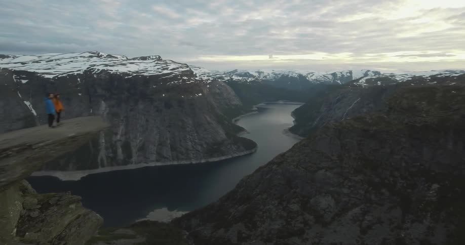 Two people are standing by the edge of a cliff looking over the edge