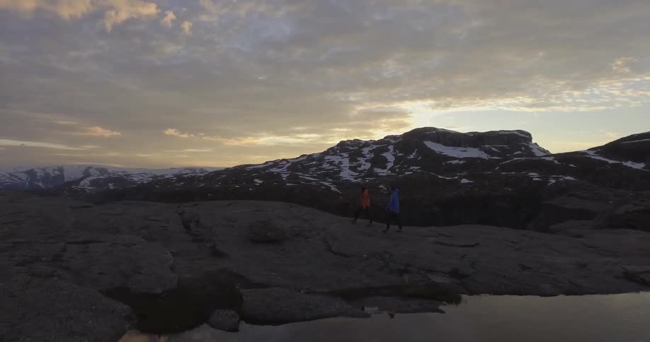 Two people are hiking on a rock covered area at sunset