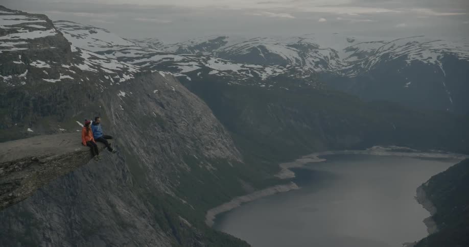 Two people are sitting on the edge of a rock over a cliff