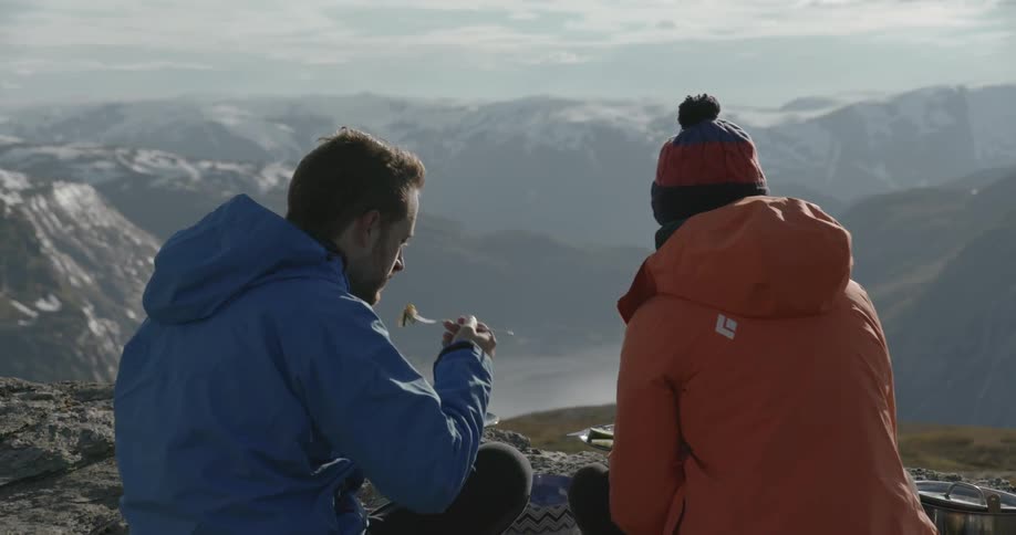 A man and a woman eat near a cliff