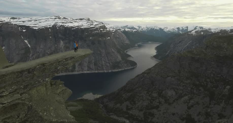 Two people are standing on the edge of a cliff looking below