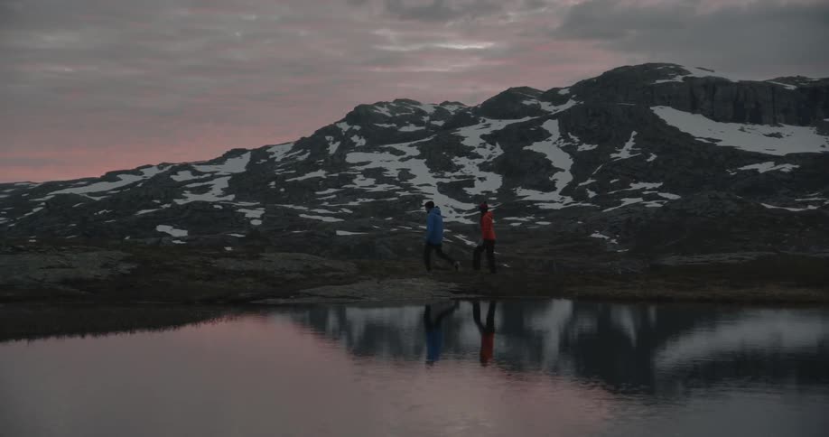 Two people walk near a lake at sunset