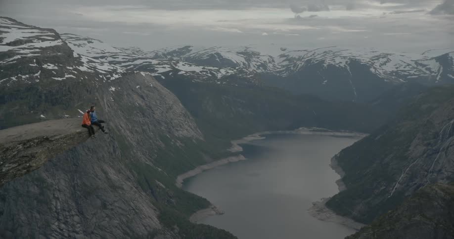 Two people sit on the edge of a cliff