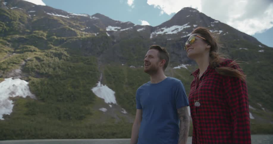 A man and woman stand and talk near a snowy mountain